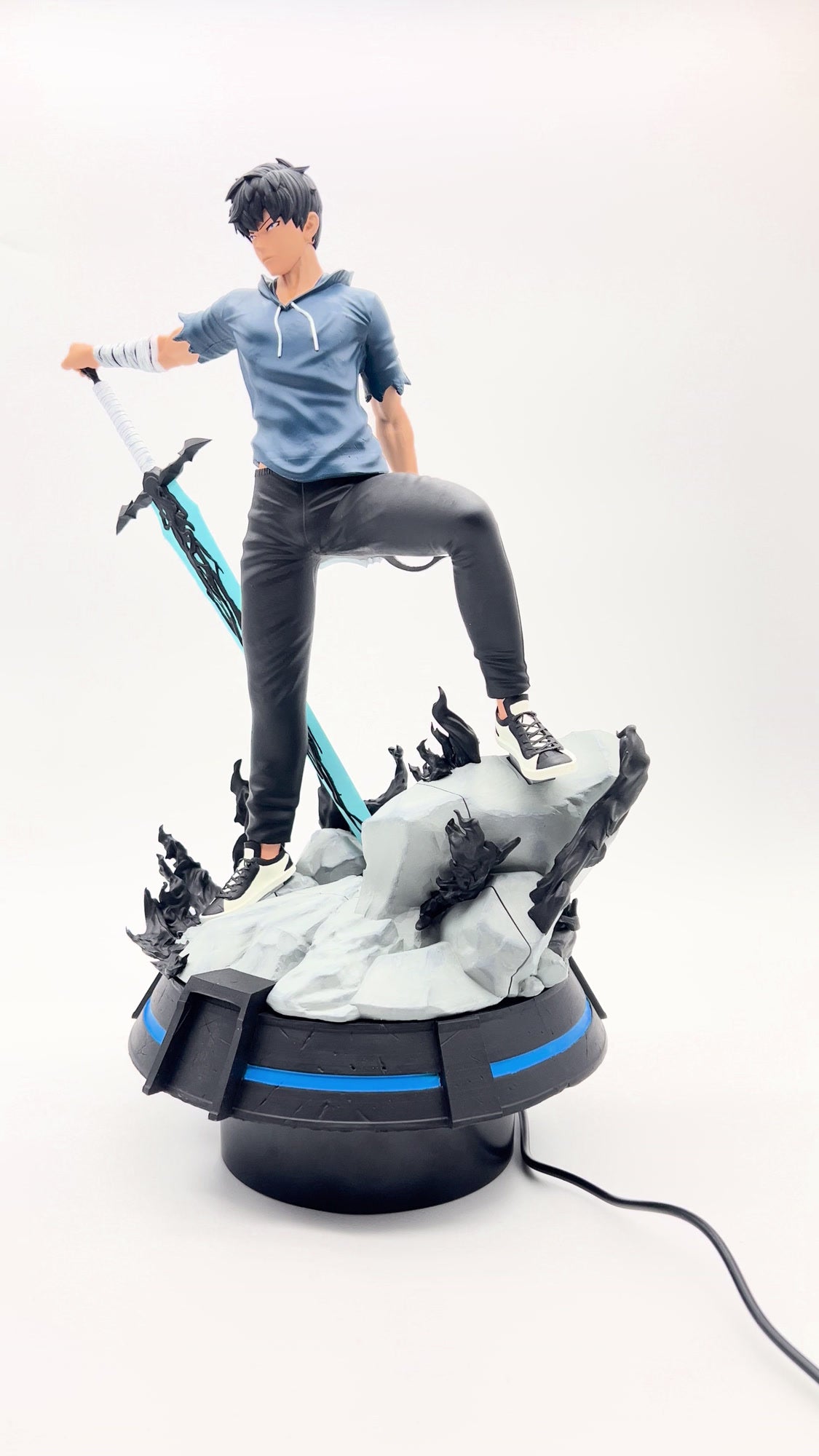 Hand-painted Sung Jin-Woo resin figure in a blue hoodie, holding a blue sword on a rocky base, by Cured Cove